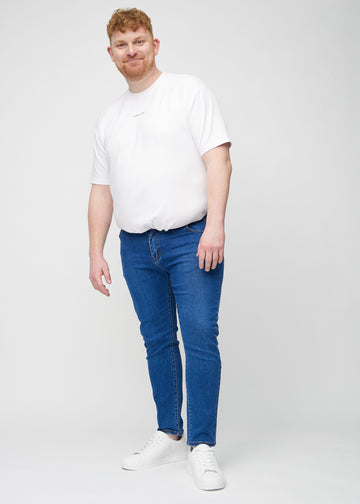 Full-length view of a plus-size model in dark blue denim slim jeans.