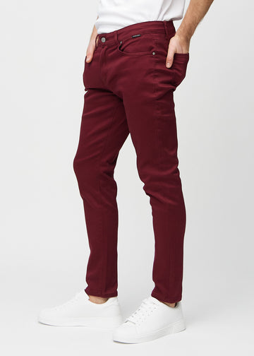 Dark red slim jeans viewed from the side on a model.