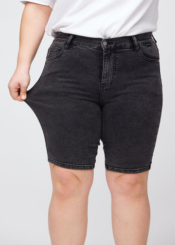 Plus-size model strækker shortsene ved låret for at vise stretch.