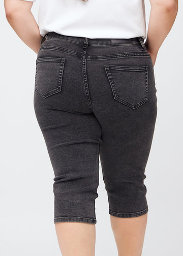 Tæt billede af bagdelen på en plus-size model i mørkegrå denim slim capris – detaljefokus på lommer og syninger.