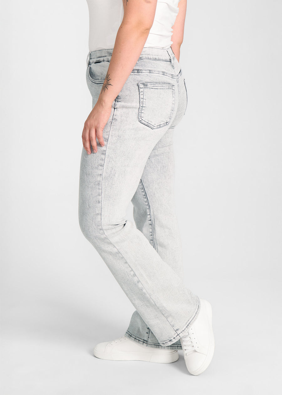 Lysegrå denim bootcut jeans, modelnavn Ashes, som sidder tæt om hofter og lår med et let svaj fra knæet og ned, set fra siden på model på en plus-size model.