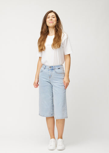 Model viser løse, lyseblå denim capris i farven Waves i bevægelse og demonstrerer pasform og materiale.
