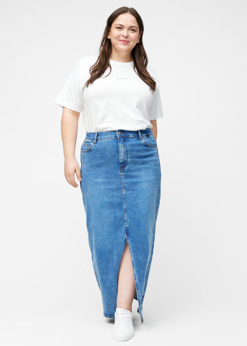 Plus-size model viser lang, klassisk blå denimnederdel i farven Rivers med regulær pasform i bevægelse og demonstrerer slids og materiale.