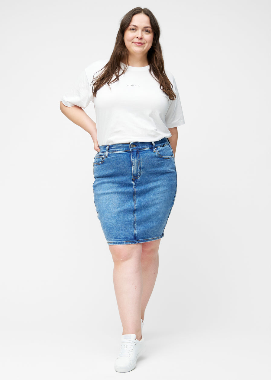 Plus-size model viser klassisk blå, tætsiddende og knælang denimnederdel i bevægelse og strækker materialet.
