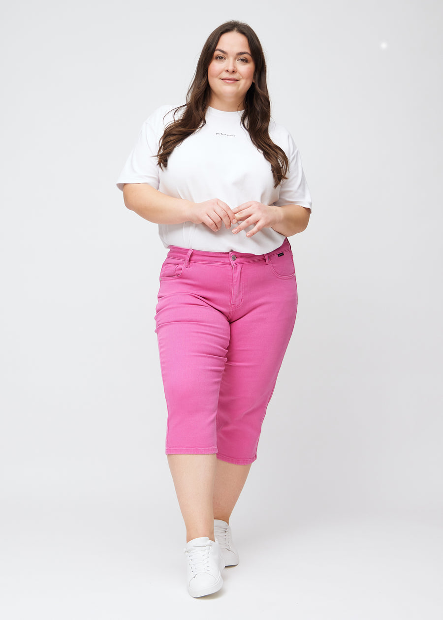 Plus-size model går ind i billedet, strækker i sine lyserøde slim capris, drejer rundt for at vise dem frem og forlader derefter billedet.